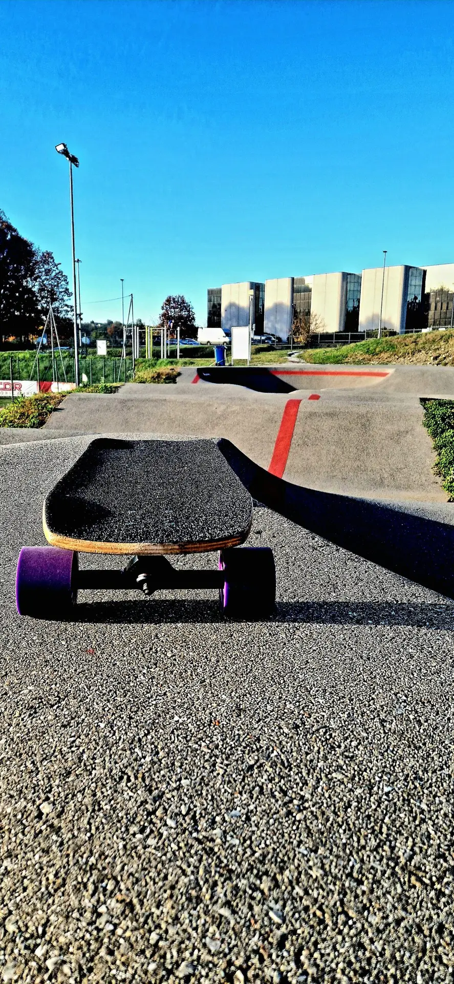 Skateboard appoggiato su una pumptrack con curve paraboliche in un impianto sportivo all’aperto.
